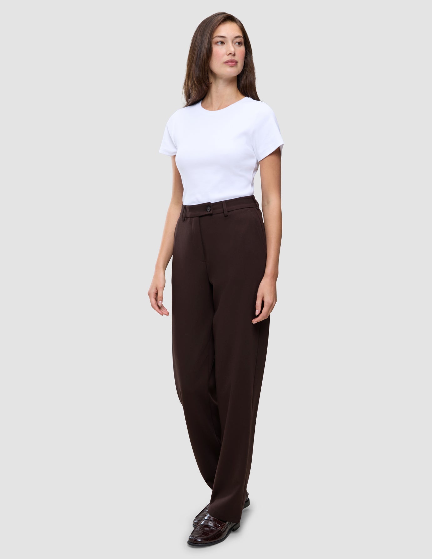 En kvinne kledd i en hvit T-skjorte, Women GO2 Pants Straight Mocha i rett passform og loafers.